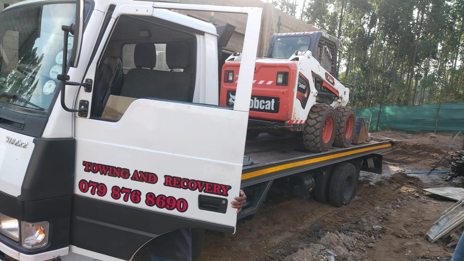 Bobcat equipment being transported on flatbed tow truck